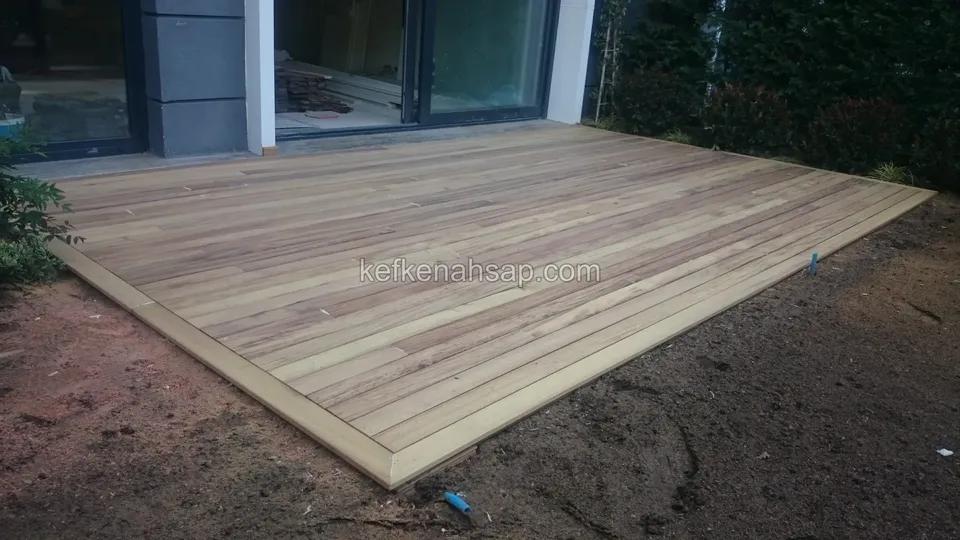 Light brown timber deck floor laid in front of glass doors, with bare soil still around it