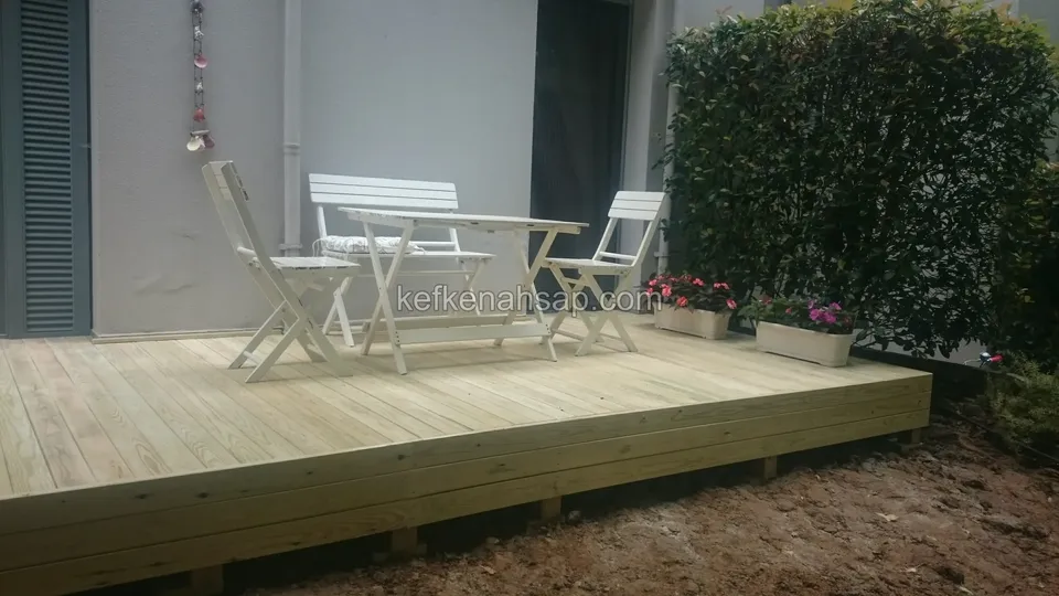 White folding table and chairs on a light timber deck, with small planters along the edge