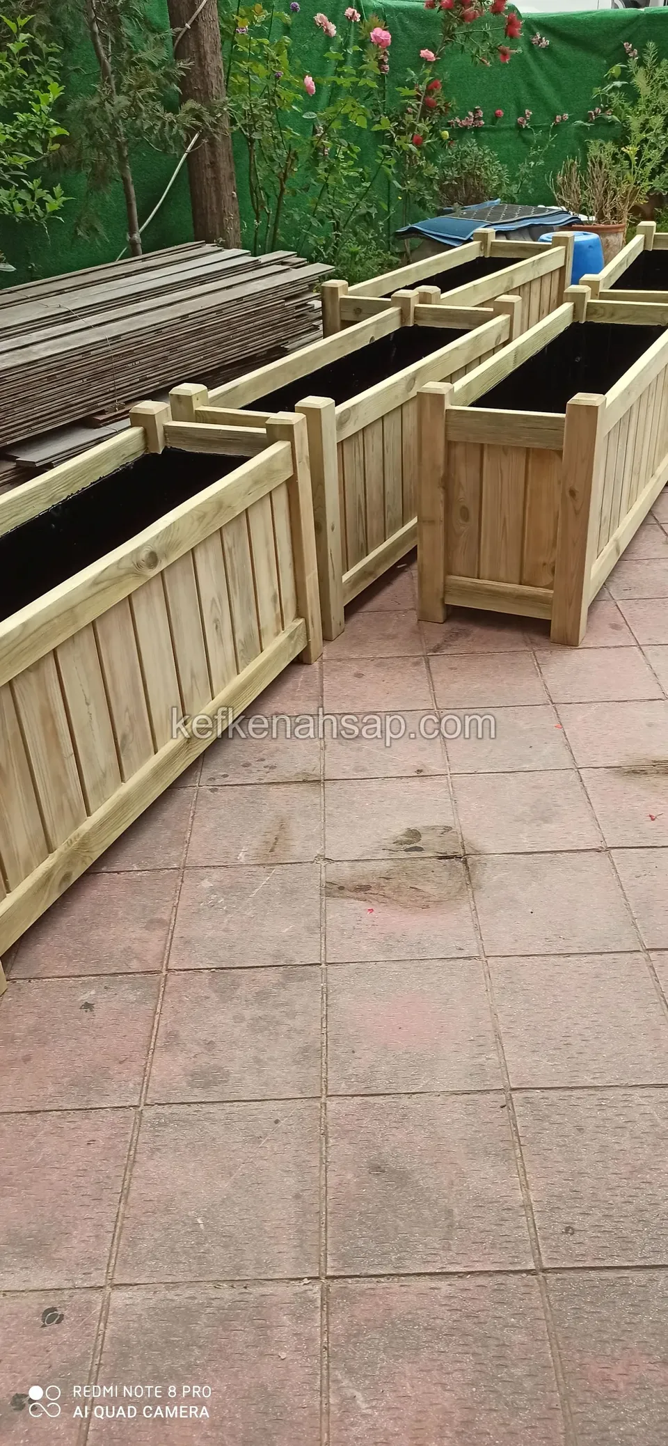 Light timber planters with vertical boards lined up on a tiled floor, with a pile of timber behind