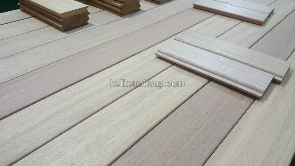 Açık krem tonlu ahşap deck tahtalarının üzerine bırakılmış iki profilli kenar parçası ve köşede koyu bir parça