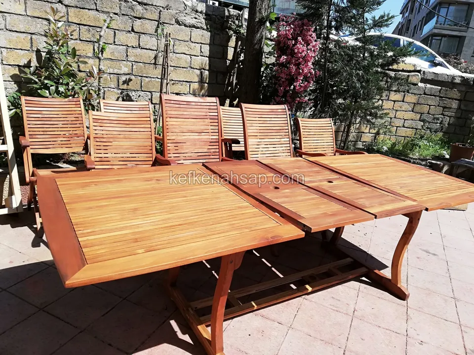 Holzesstisch mit Latten und ausgeklappten Verlängerungen sowie Klappstühle im Hof mit Steinmauer