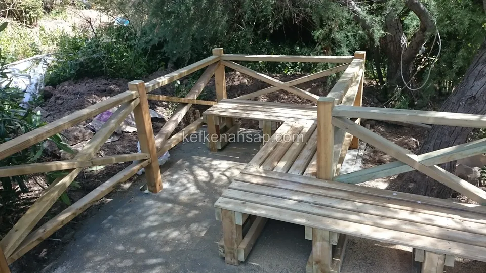 Ağacın altındaki bahçe yolunda, çapraz korkuluklarla çevrili köşe oturma bankı