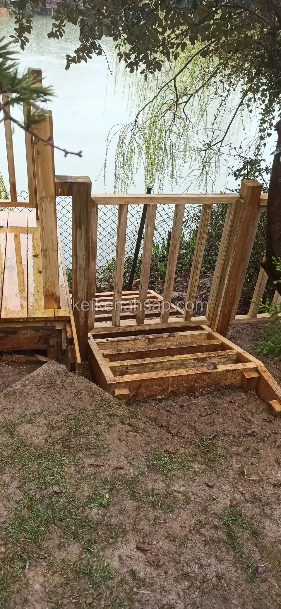 Railed deck under a tree at the lakeside with a timber step set on the soil