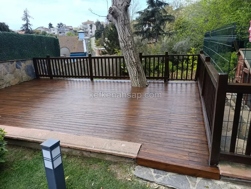 Dark brown wooden garden deck built around a tree trunk, with a vertical-slat wooden railing along its edge