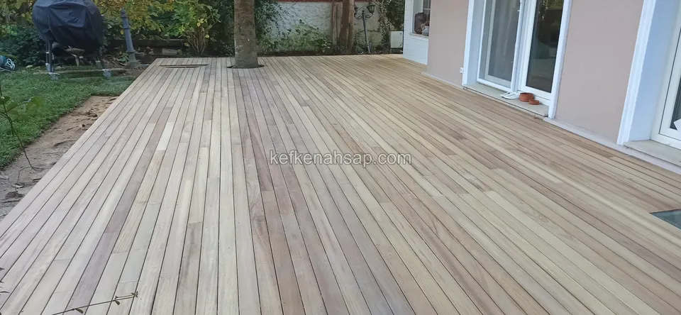 Ağaç gövdesi ve cam kapılar yanında geniş, açık renkli deck zemini, boydan boya uzanıyor