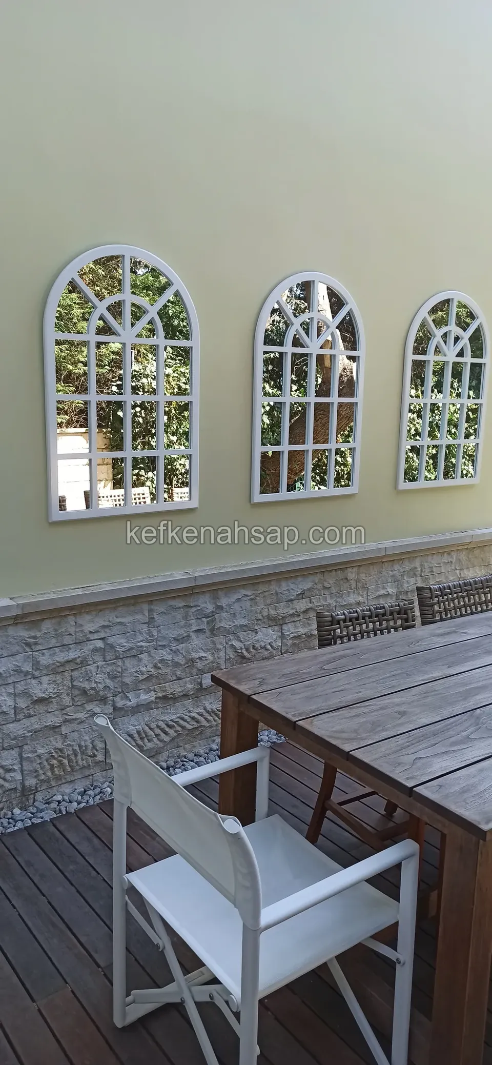 Wooden dining table and chairs on a wood deck with arched decorative mirrors on the wall.