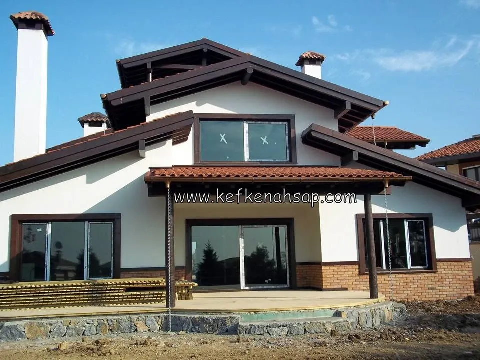 Müstakil evin kiremit çatısı altında koyu renk ahşap saçaklar, pencere pervazları ve veranda sundurması.