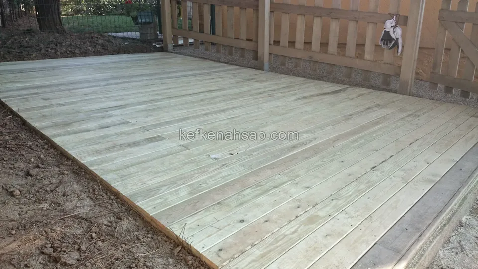 Ahşap çitin önünde, toprak kenarlı yeni döşenmiş açık renkli emprenyeli çam deck