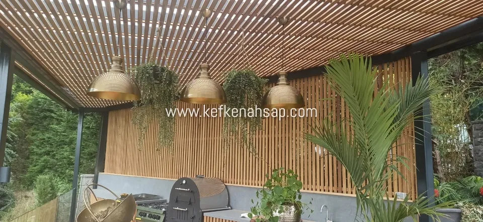 Açık mutfak ve mangal alanının üzerinde ahşap çıtalı tavan gölgeliği, çıtalı arka panel ve pirinç sarkıt lambalar.