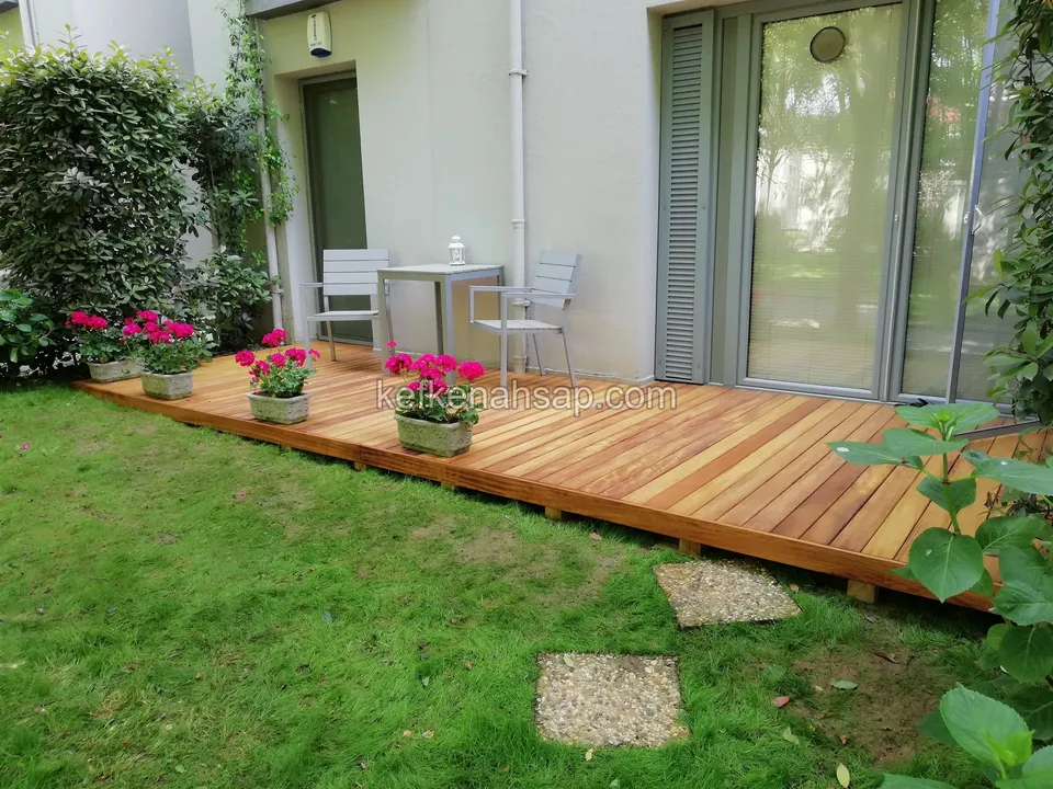 Small table, two chairs and a row of flower pots on a timber deck, with lawn and stepping stones in front