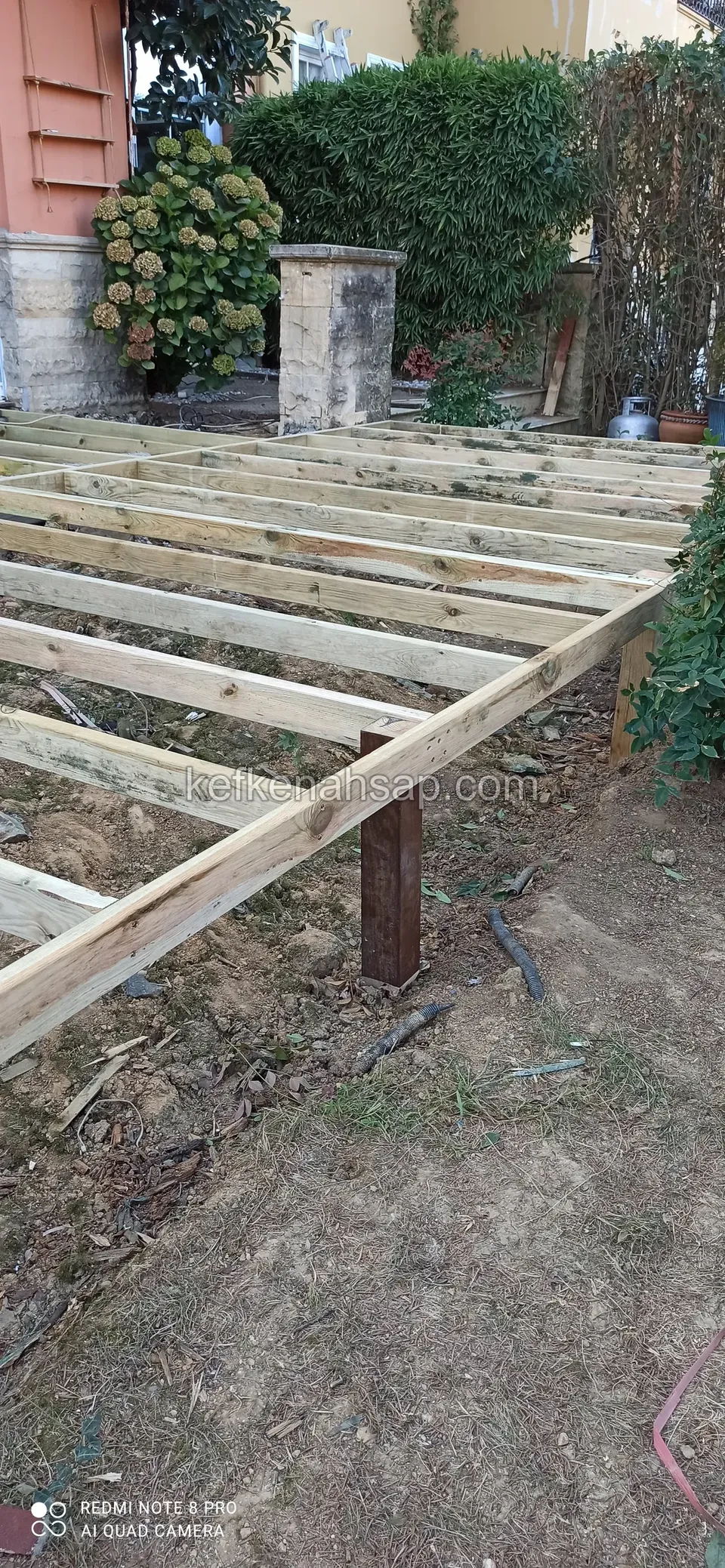 Geneigte Deckbalken auf einem Holzpfosten über Erde, mit waagerechtem Rahmen und einem Steinpfeiler dahinter