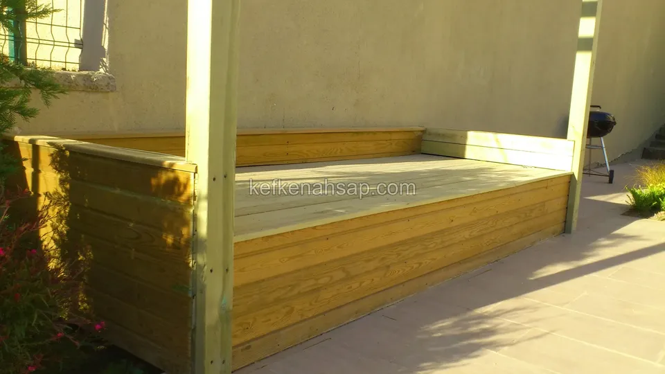 Eine mit hellgrün imprägnierten Kiefernbrettern verkleidete Sitzeinheit mit Holzpfosten vor einer hellen Wand