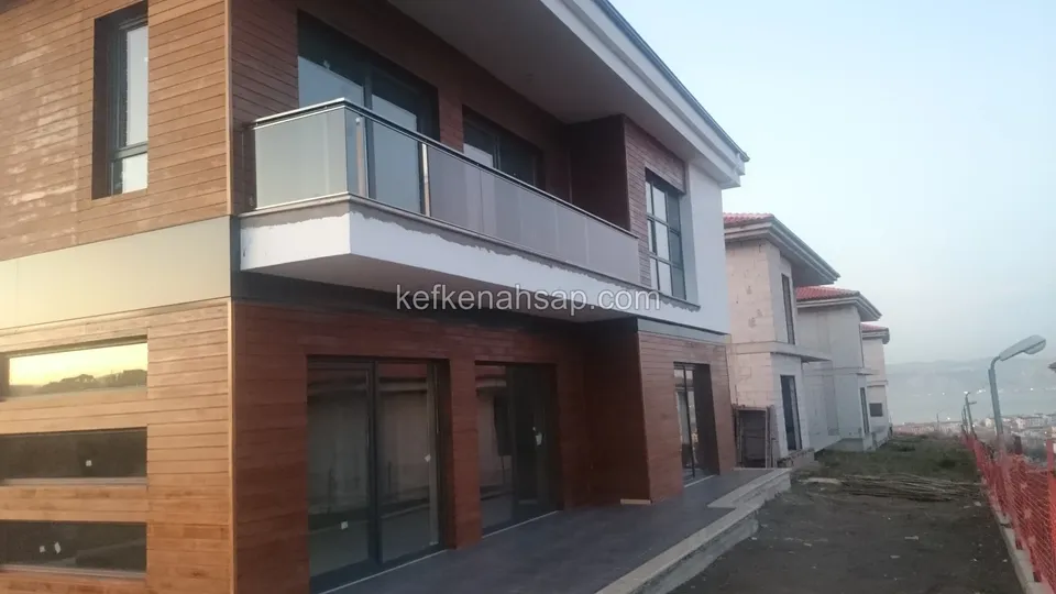 Kırmızımsı dikey ve yatay ahşap kaplamalı iki katlı modern bir evin cephesi, camlı balkon korkuluğu ve büyük cam kapılar