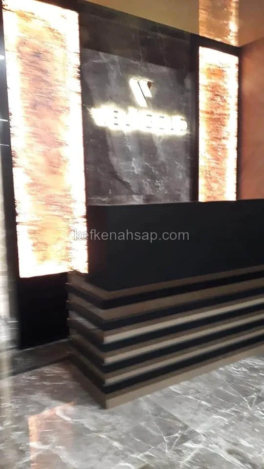 Işıklı duvar paneli önünde basamaklı ahşap çıtaları olan siyah danışma bankosu.
