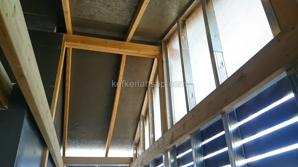 Decke mit dunkler Dämmung zwischen Holzbalken und Jalousielamellen des seitlichen Fensters
