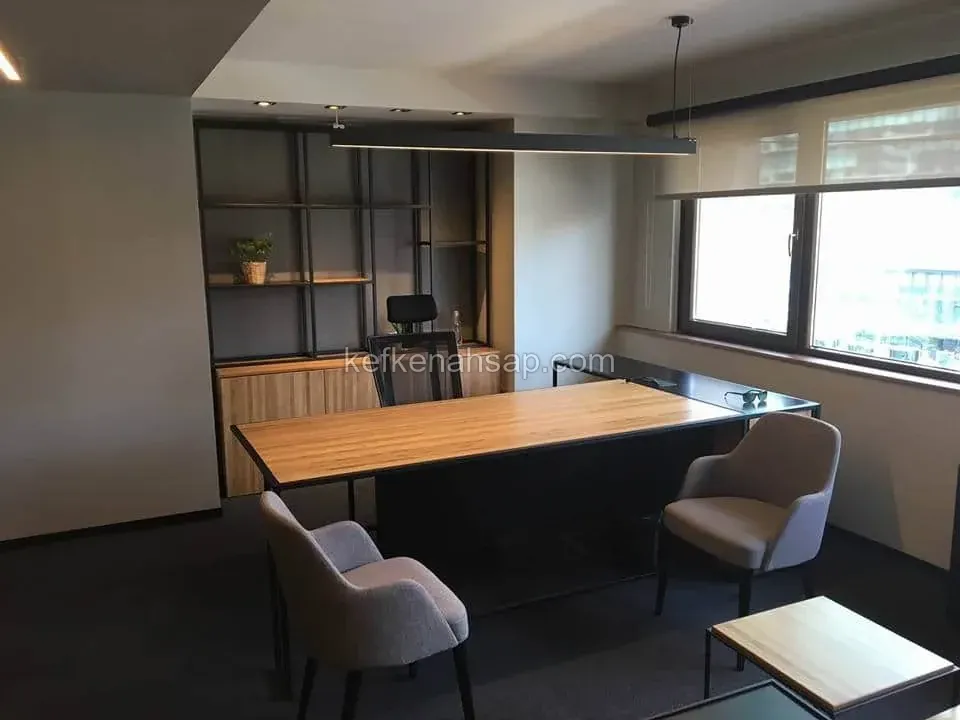 Modern ofis odasında siyah metal iskeletli ahşap çalışma masası, arkasında kitaplık ve koltuklar.