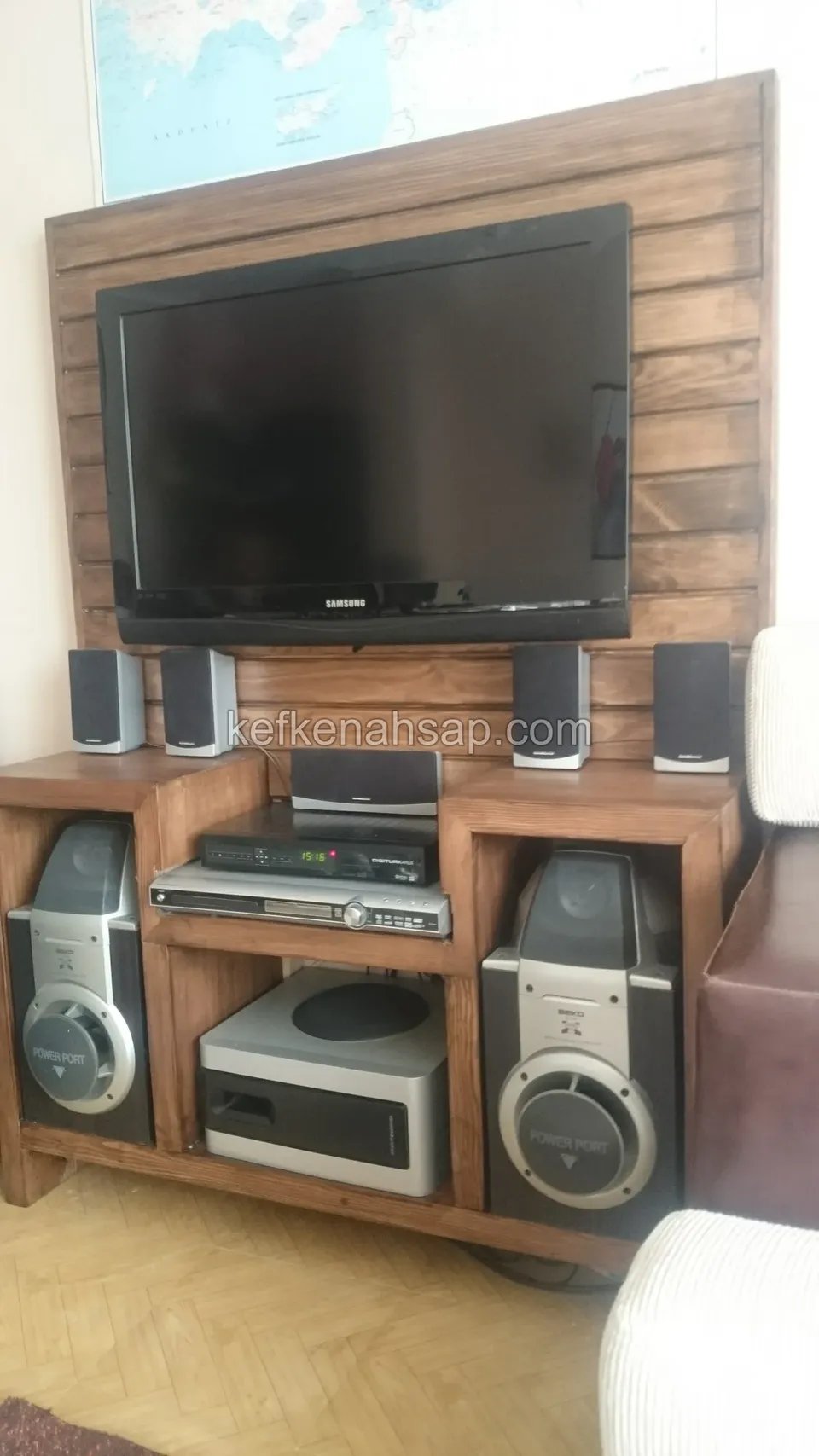 Yatay ahşap paneli olan TV ünitesi; alt gözlerde müzik seti ve hoparlörler, üstte kapalı televizyon