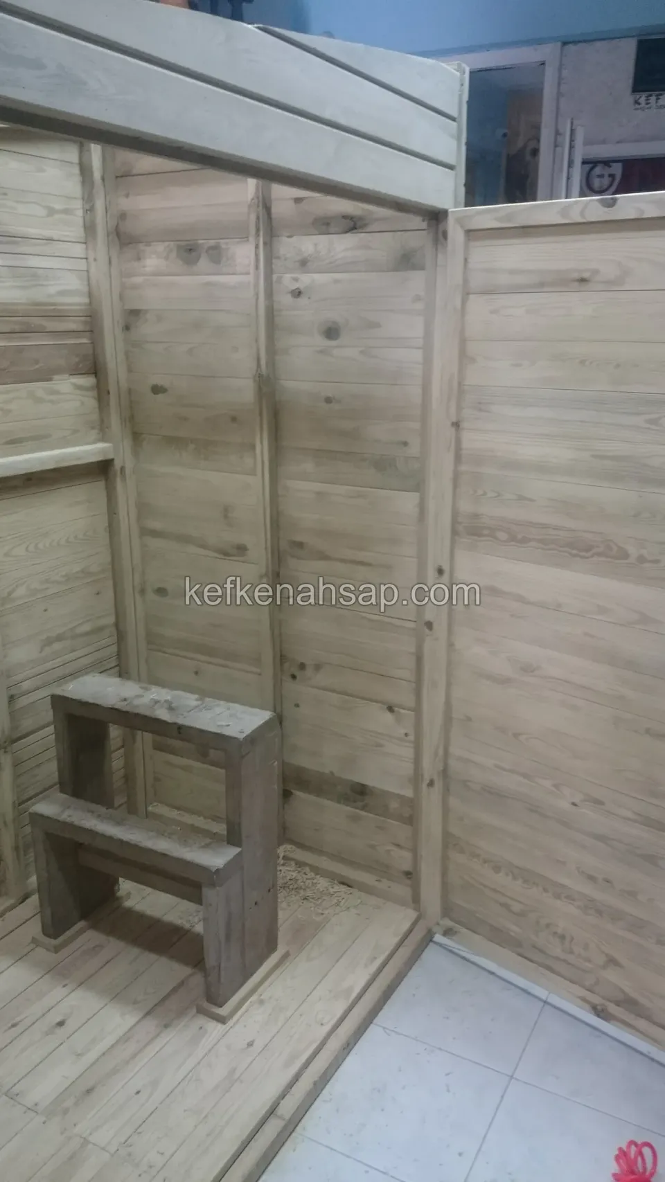 Yatay ahşap panolarla kaplı küçük kabinin içi; köşede iki basamaklı ahşap oturak, zeminde seramik var