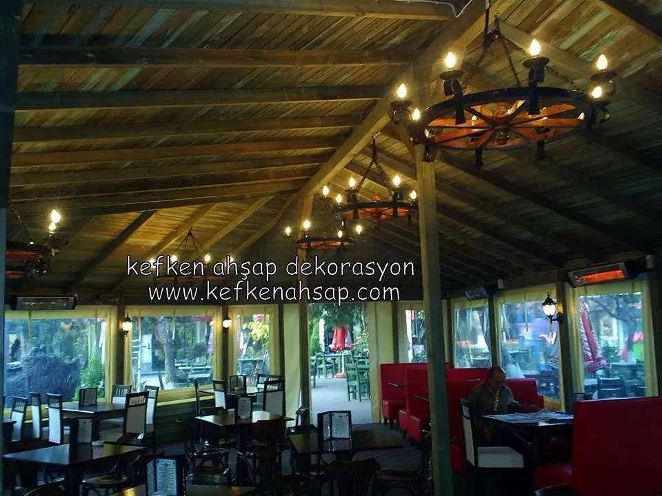 Ahşap karkas çatılı ve tekerlek avizeli restoran tavanı ile masa düzeni.