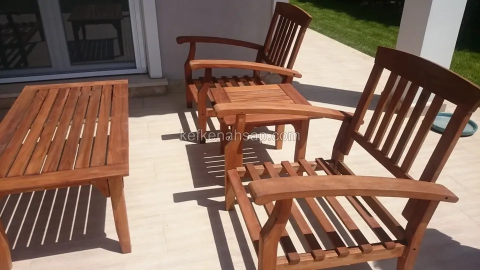 Langer Lattentisch aus Holz neben Sesseln mit Armlehnen und einem Beistelltisch auf gefliester Terrasse