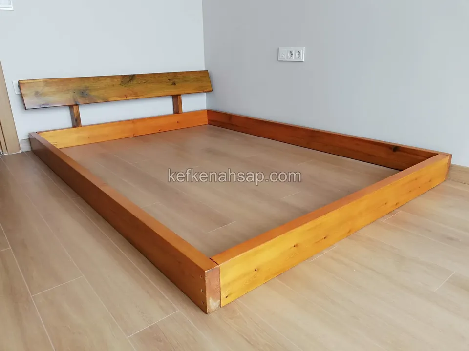 Parke zeminli odada, duvara yaslanan ahşap başlıklı alçak ahşap yatak çerçevesi