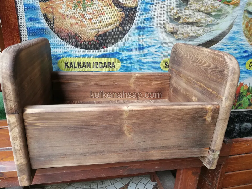 Ein Holzsessel mit hohen Seiten und angekohltem Effekt auf einer niedrigen rötlichen Bank über einem Mosaiksteinboden