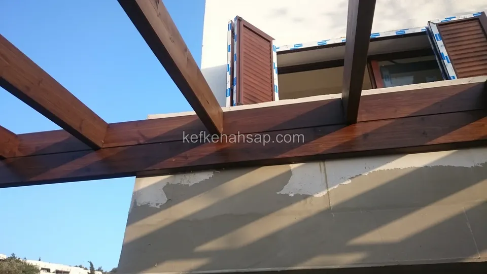 Sıvalı balkonun yanında vernikli pergola kirişleri, çapraz payandalar ve üstte panjurlu pencereler