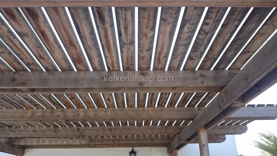 Alttan görünen çıtalı ahşap pergola çatısı, koyu tonlu kirişler ve çıtaların arasından süzülen gökyüzü