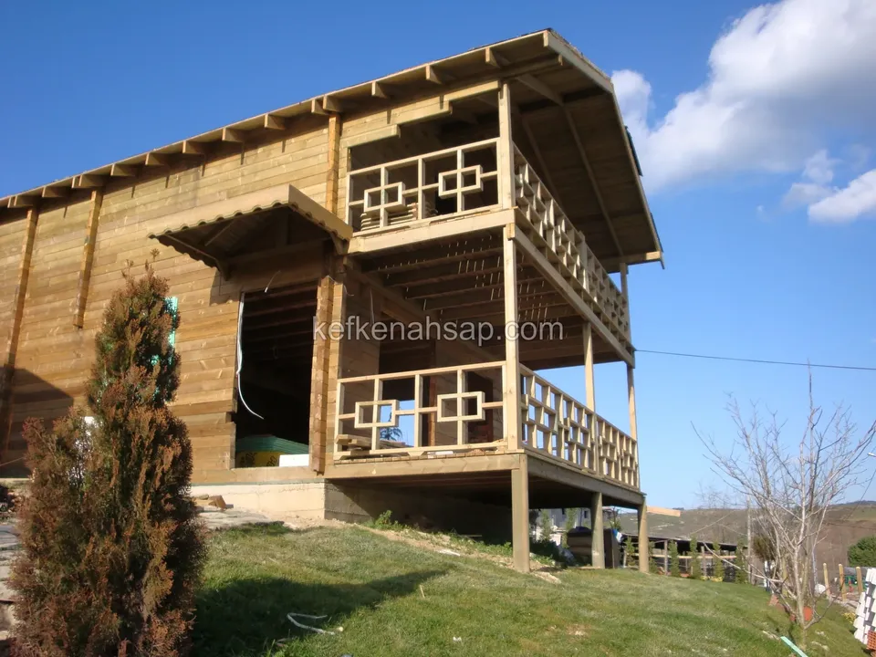Çimli yamaçtan görünen, geometrik desenli balkon korkuluklarıyla iki katlı ahşap ev