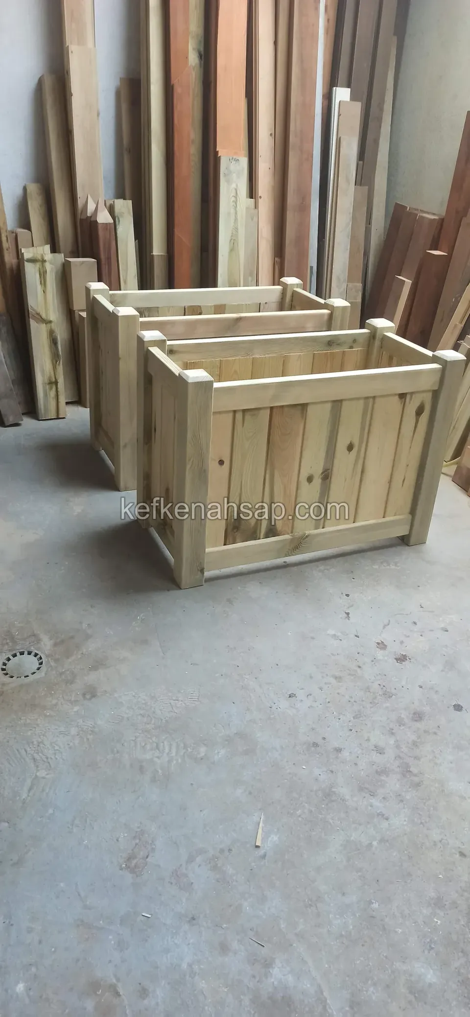Two light timber planters on the workshop floor with timber stacked upright behind