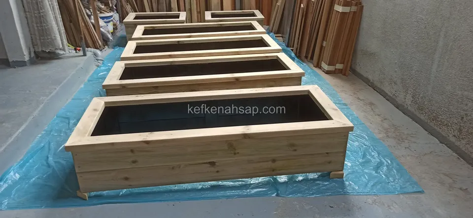 Five long timber planters lined up side by side on blue plastic on the workshop floor