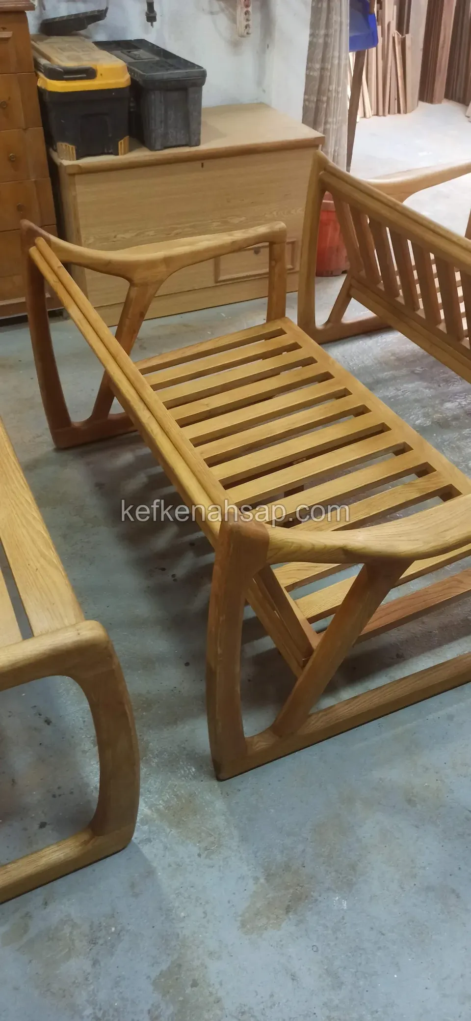 Çıtalı oturaklı, kollu ve kızak ayaklı ahşap kanepe iskeleti, arkada atölye eşyaları