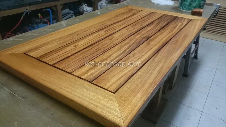 A rectangular golden-brown varnished timber table top on a workshop bench