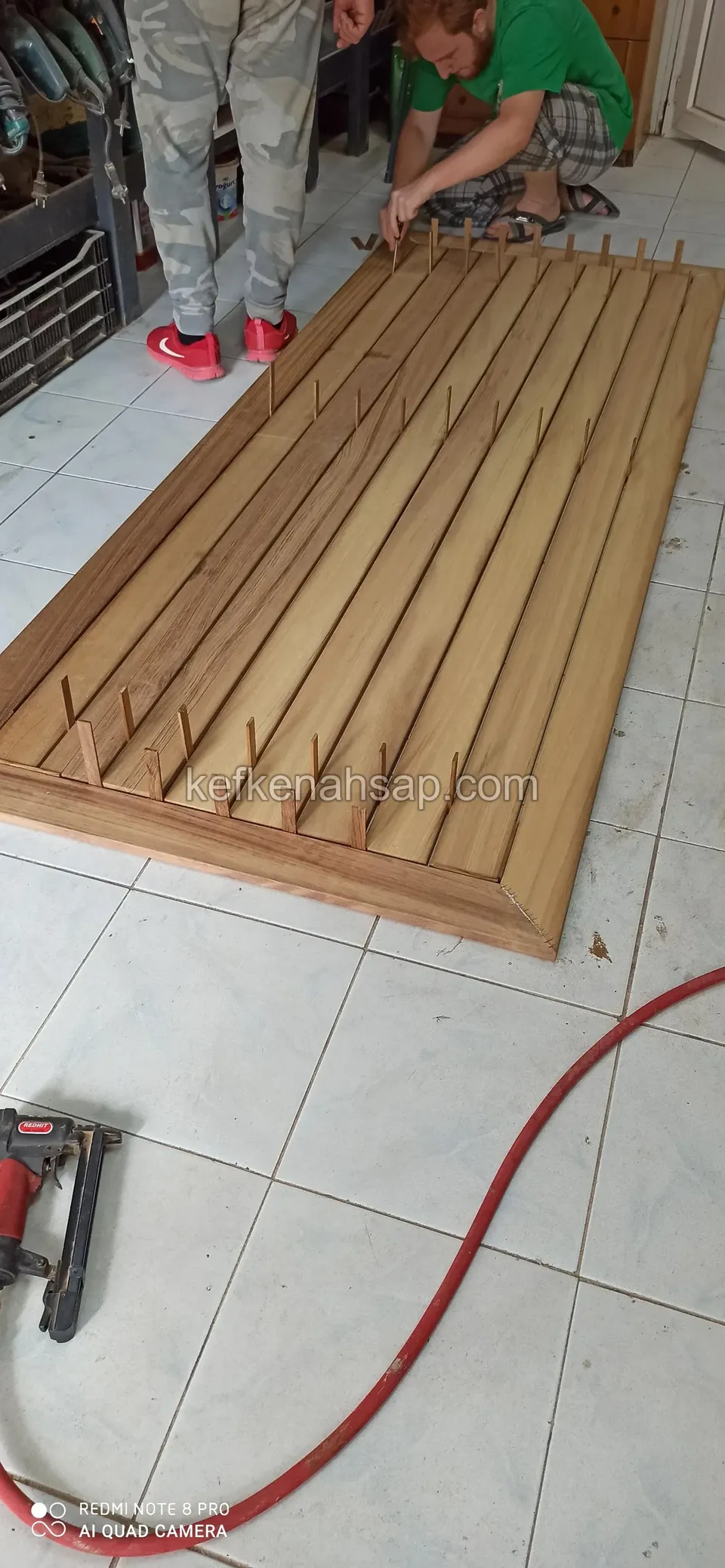 A deck panel being assembled on a tiled workshop floor, with slats laid out and a nail gun and air hose beside it