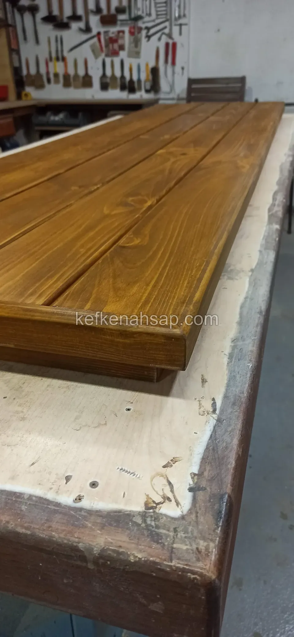 Atölyede kalın bir ahşap masa tablası, arka duvarda alet panosu