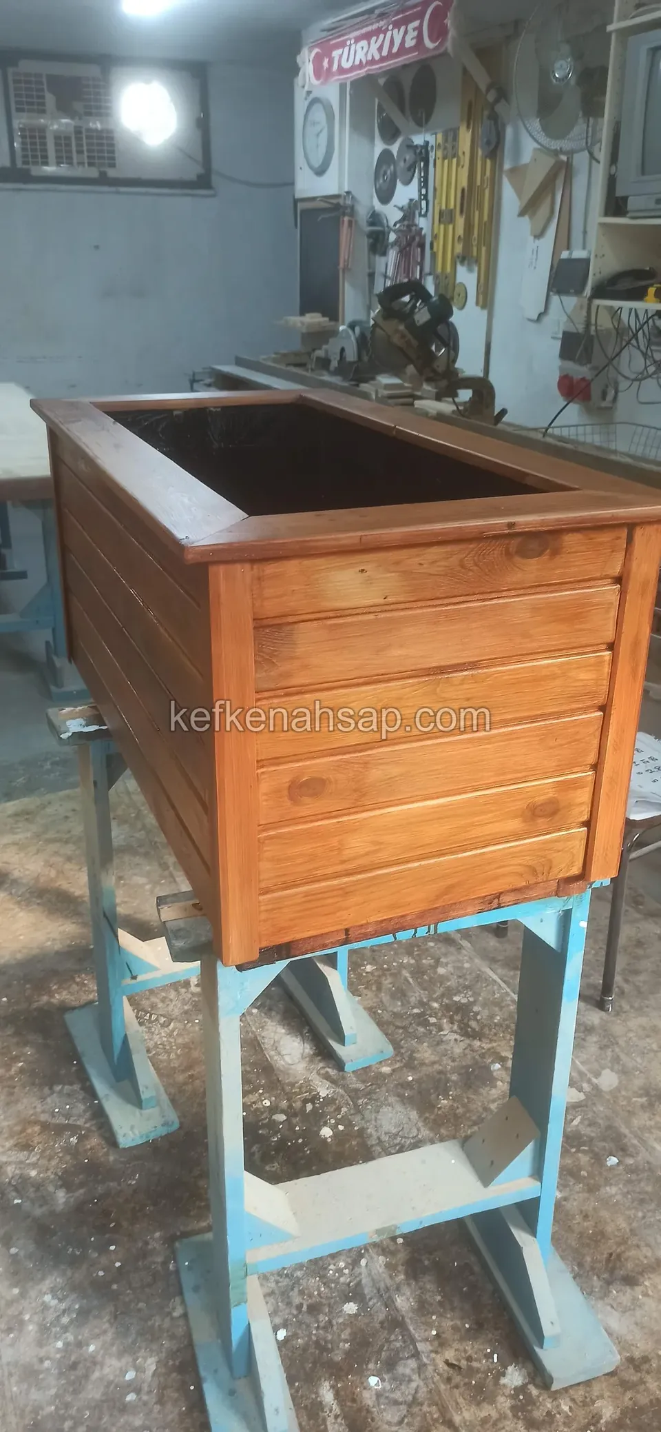 Varnished timber planter with horizontal slats set on a blue steel stand in the workshop