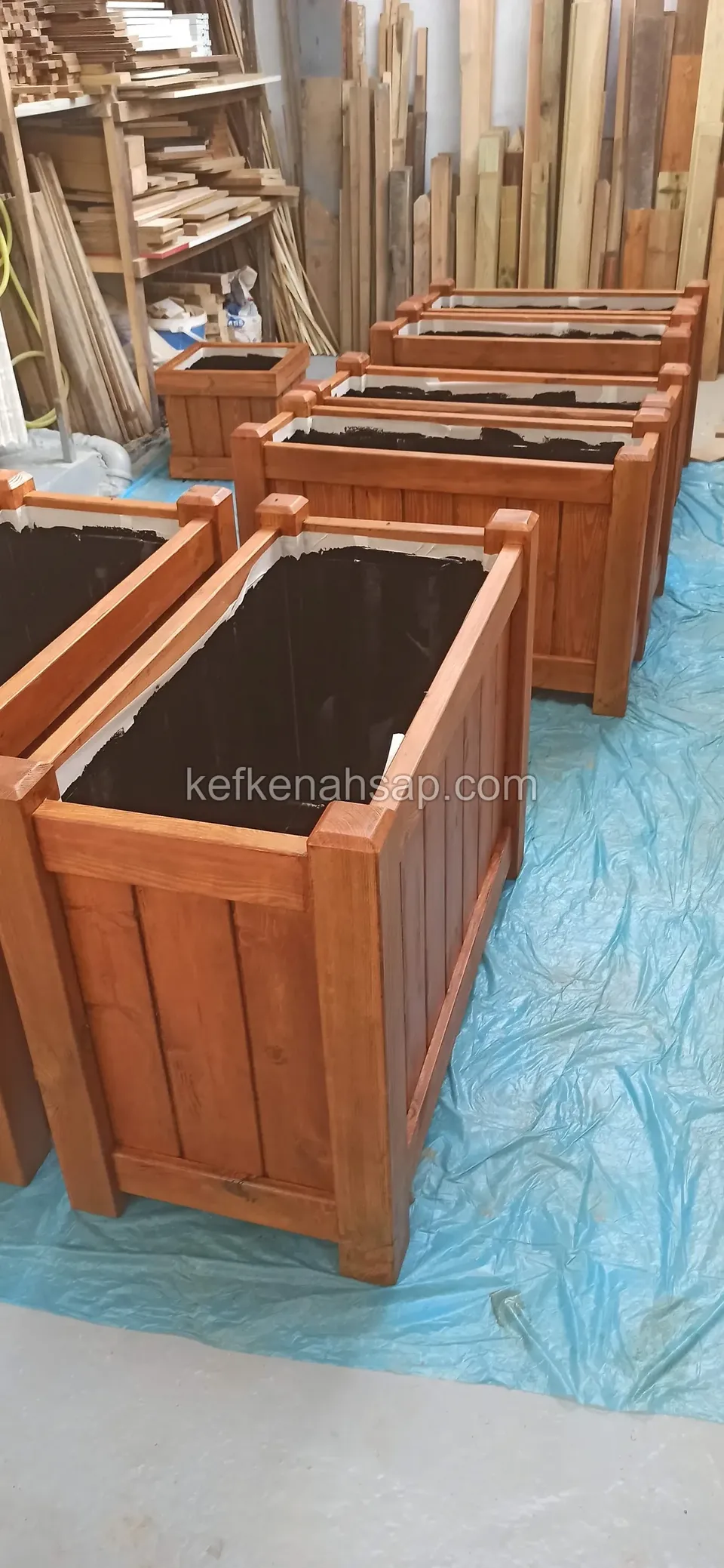 Vertical-board timber planters freshly varnished and lined up on a blue sheet in the workshop
