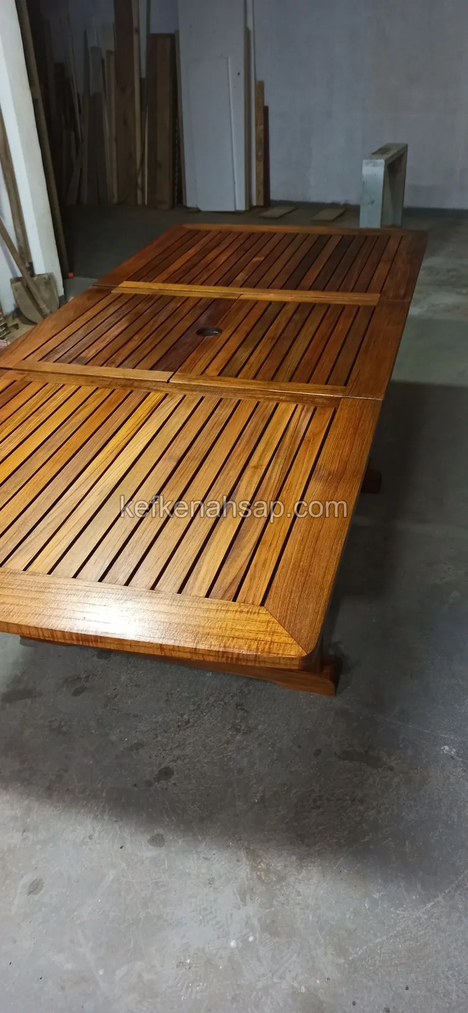 Auf dem Betonboden einer Werkstatt liegt eine Lattentischplatte aus Holz mit Ausziehplatten in glänzendem Lack