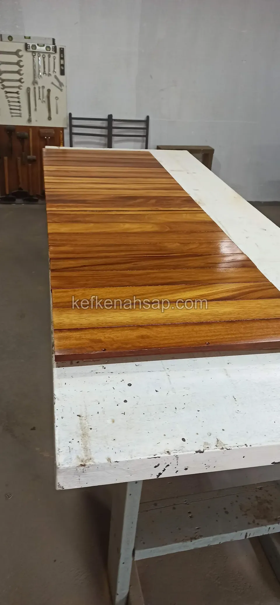 Lange glänzend lackierte Tischplatte aus Holzstücken in verschiedenen Tönen auf einer weißen Werkbank