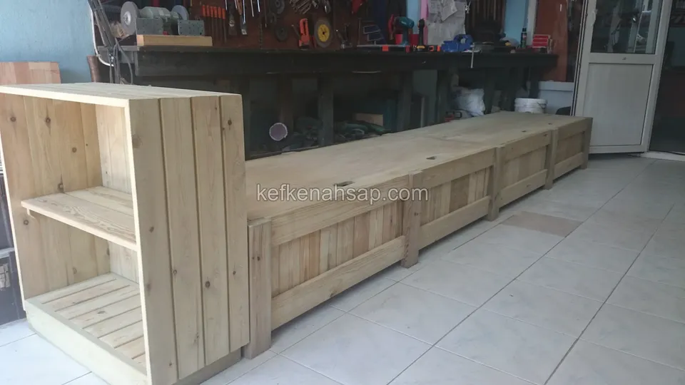 Atölyede uzun bölmeli ahşap kasa ve ucundaki raflı ünite, yandan görünüm