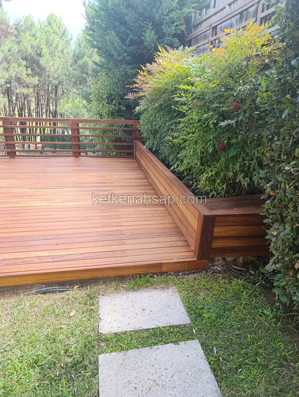Wooden decking with built-in wooden bench and railing in a lush garden setting.