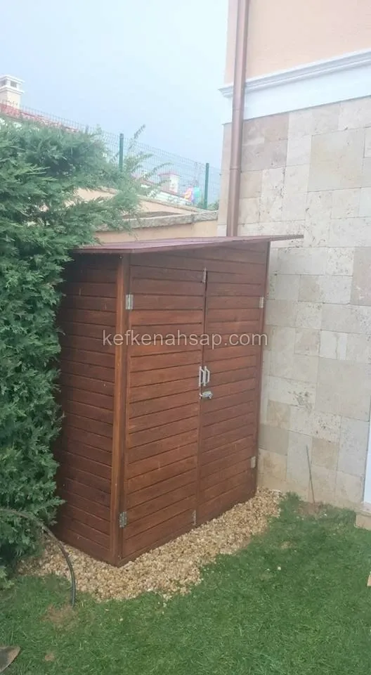 Taş kaplı villa duvarının yanında, bahçede duran koyu kahverengi yatay çıtalı çift kapaklı ahşap depo dolabı
