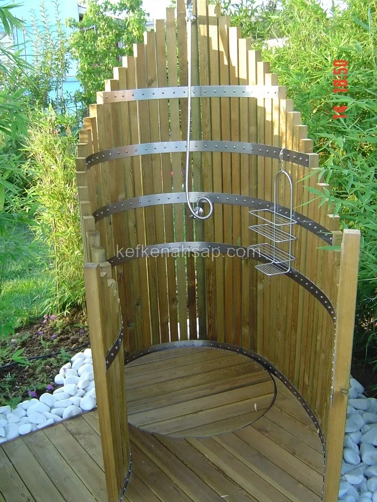 Bahçede çıta ve metal şeritlerle yapılmış yuvarlak ahşap duş kabini, içinde duş başlığı ve telli sabunluk, zemini ahşap deck