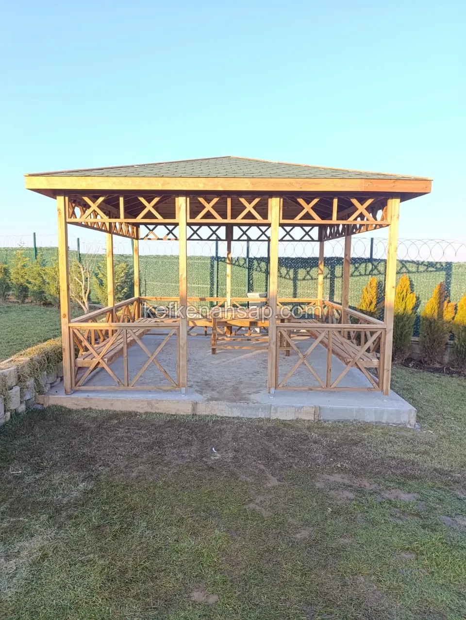 Beton kaide üzerine kurulmuş, kırma çatılı ve ahşap korkuluklu bahçe kamelyası.