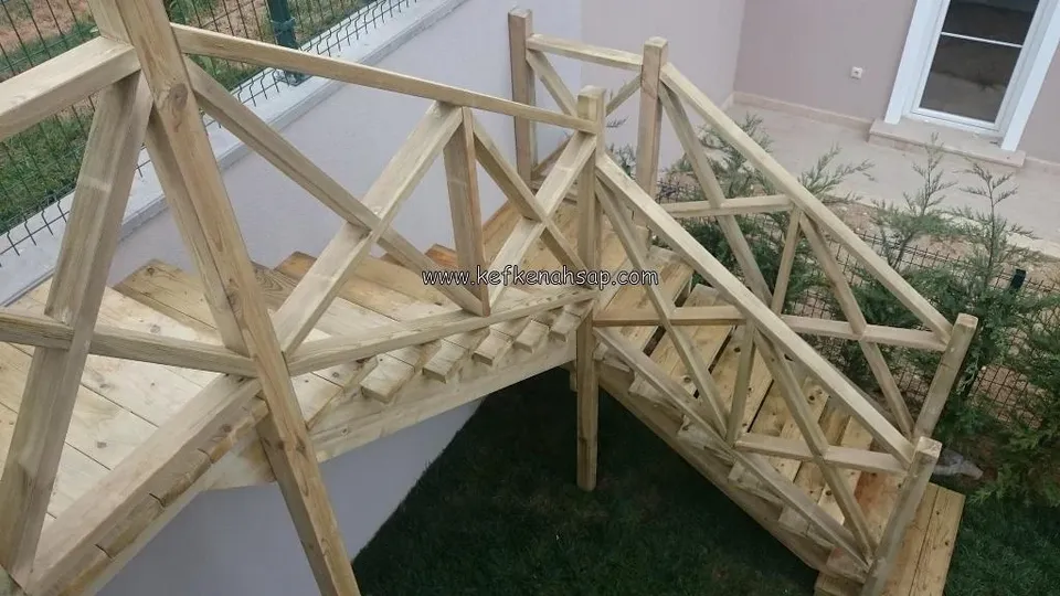 Bahçeye inen, çapraz çıtalı korkuluklara sahip dönemeçli ahşap merdiven; yanında çim alan ve villa cephesi var