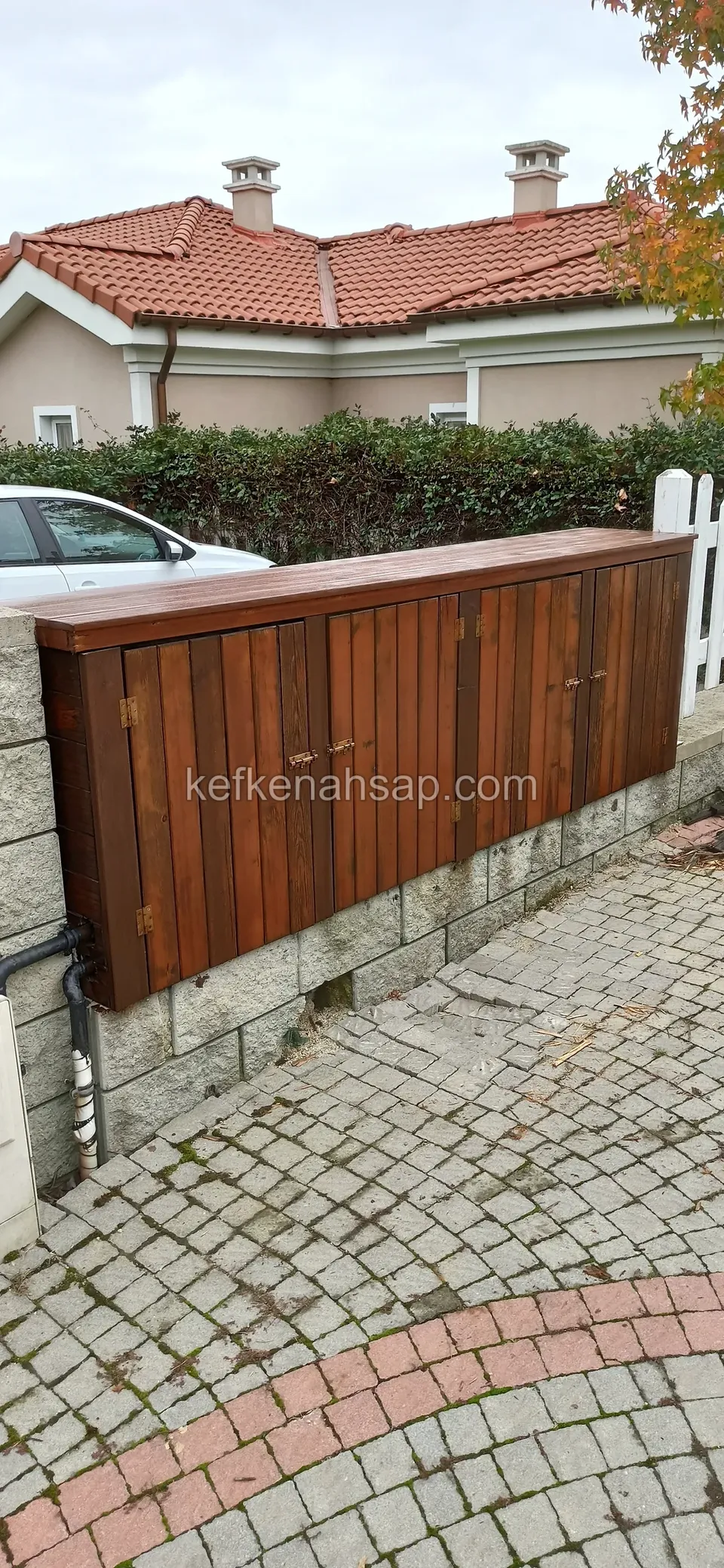 Parke taşlı yolun kenarında, bahçe duvarına oturan dikey tahtalı koyu ahşap dolap