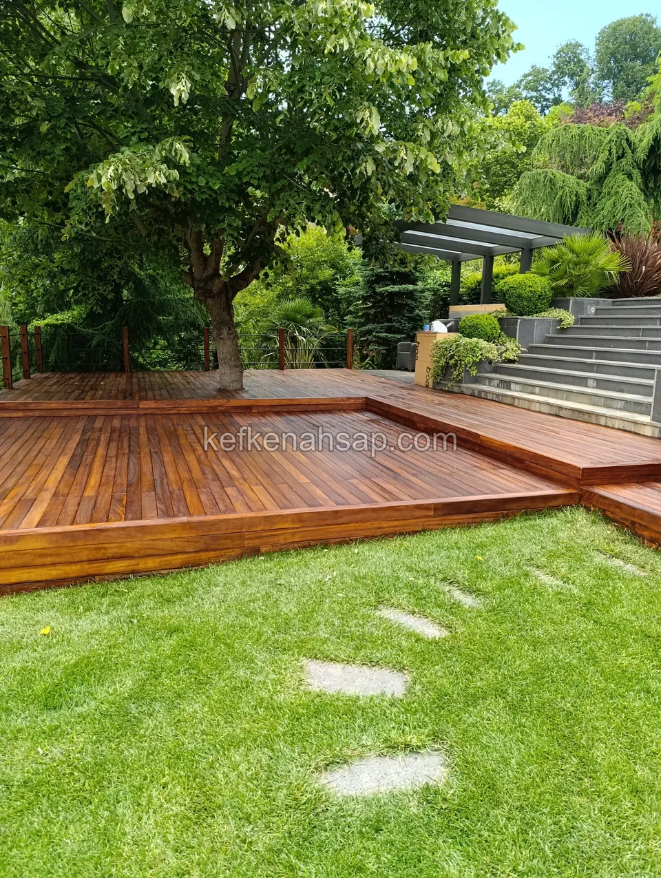 Multi-level wooden deck installed around a tree in a lush green garden.