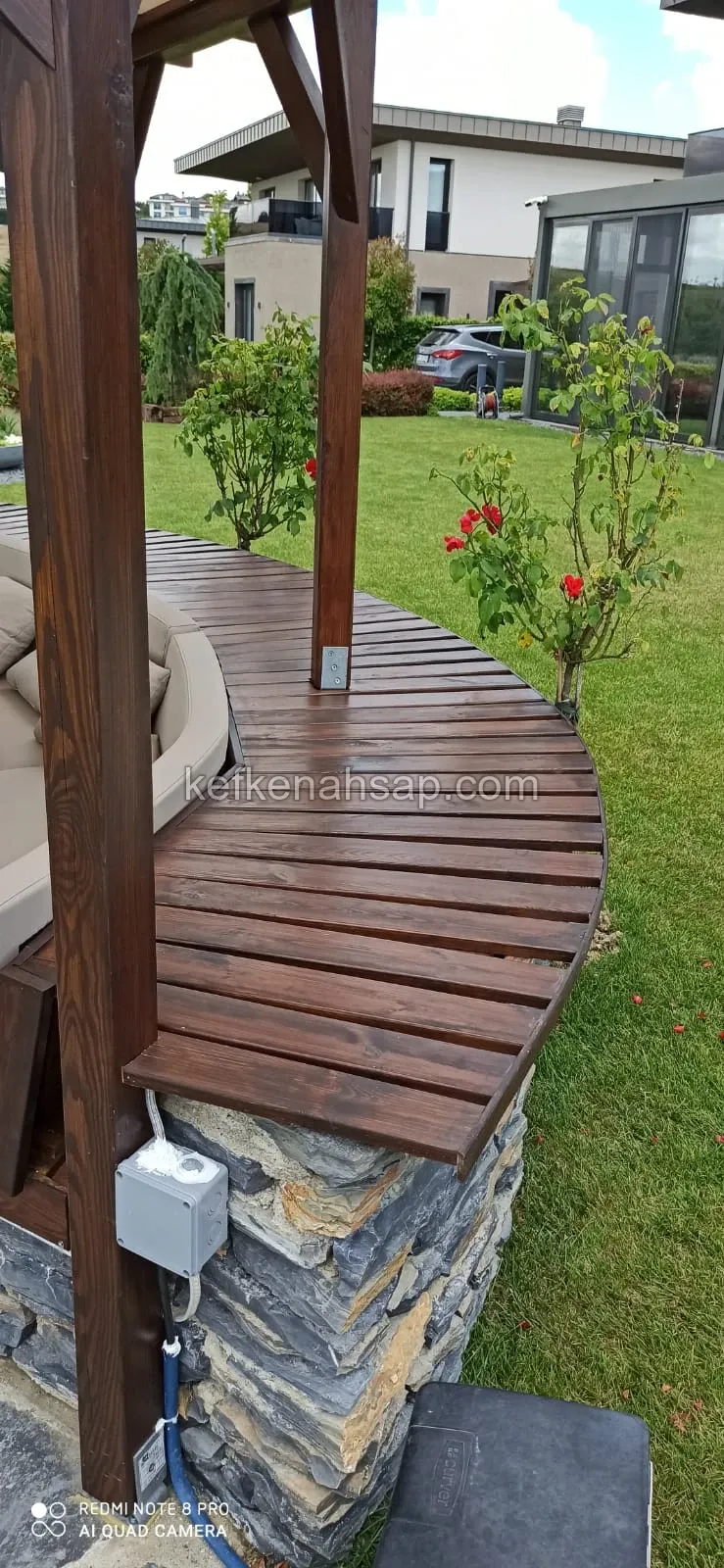 Curved wooden decking on a stone base and support posts of a garden gazebo.