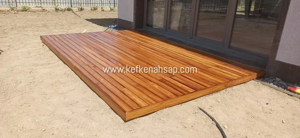 Sürgülü cam kapının önünde, çıplak toprak zemine döşenmiş bal rengi ahşap deck platform