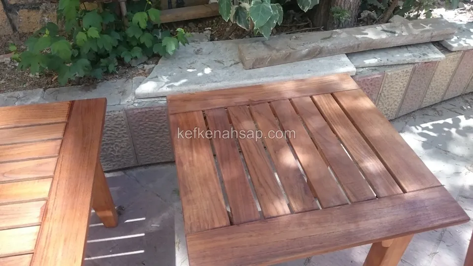 Sarmaşıkların önündeki teraste, çıtalı üstü olan kare ahşap yan masa